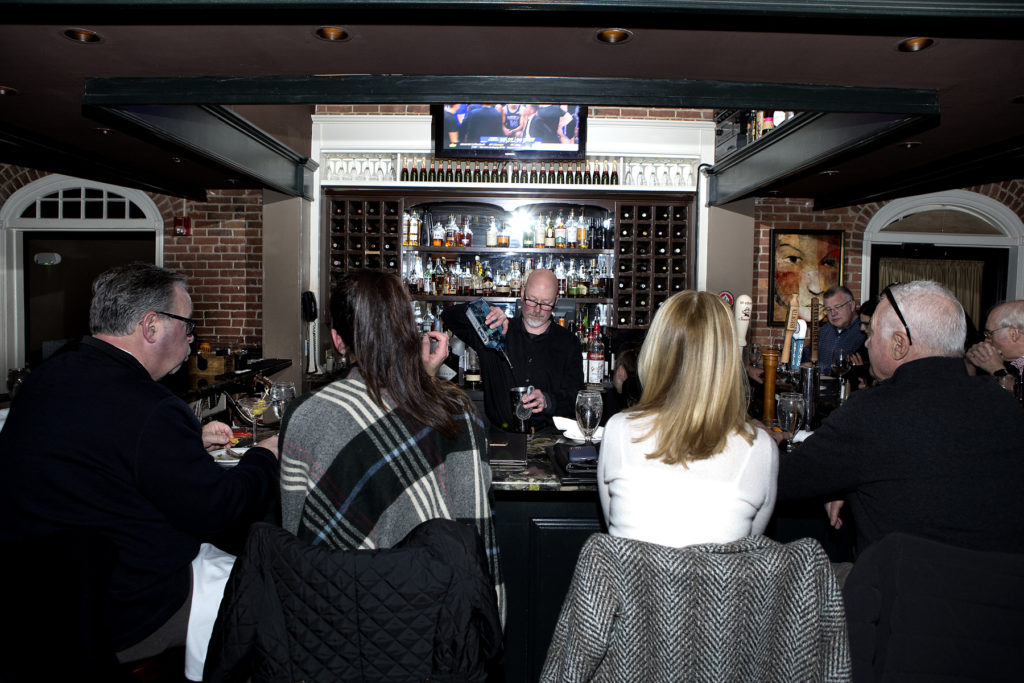 Patrons at the bar and the bartender puring drinks